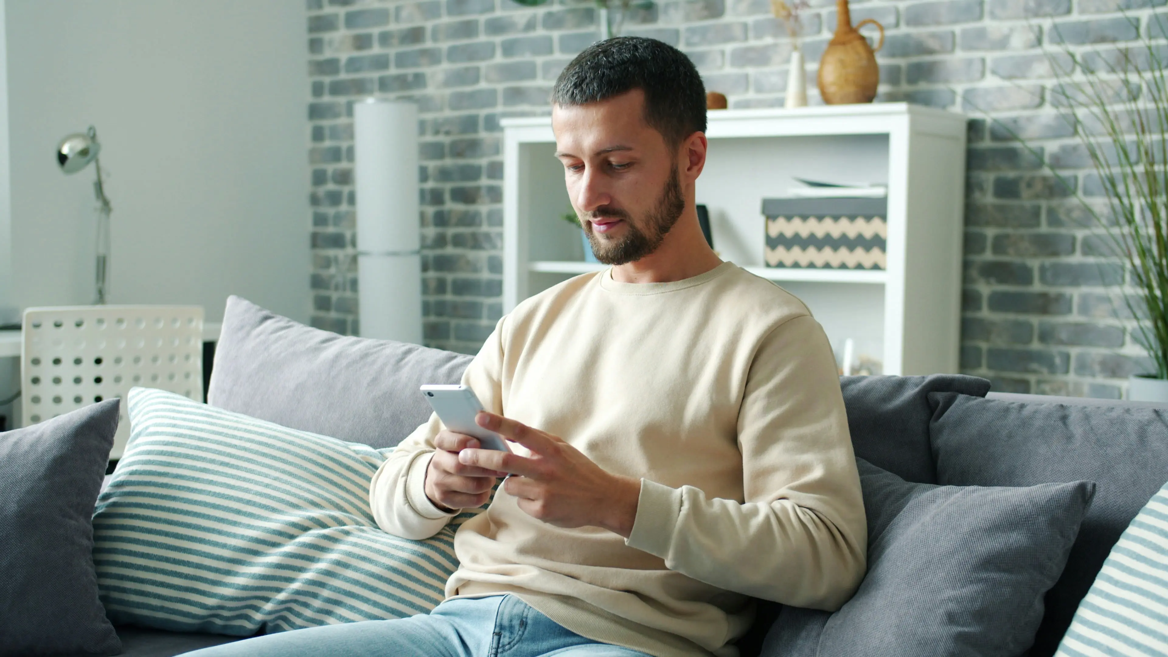 A man relaxing on a sofa, smiling as he uses his phone